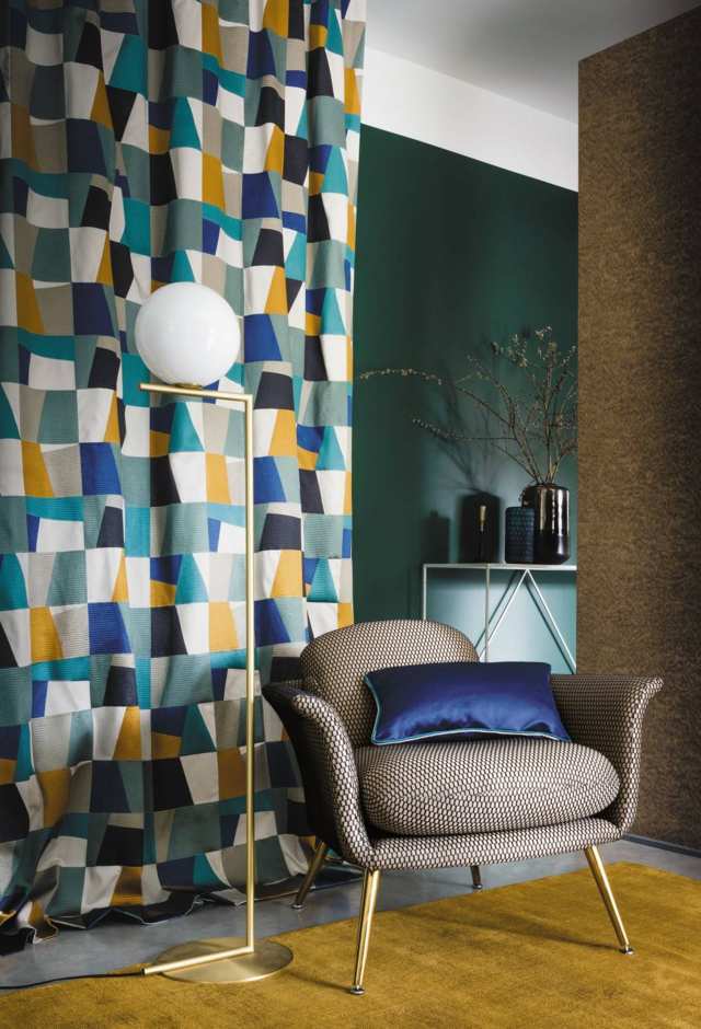 Cortinas fruncidas de rombos azules y marrones estilo vintage delante hay una butaca marrón y una lámpara de pie dorado con bola blanca en la punta